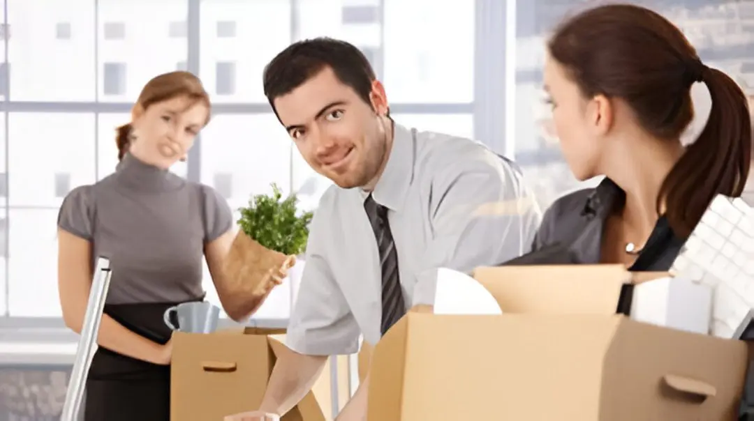 Office workers packing boxes, smiling, moving day.